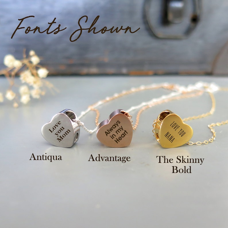 May include: Three silver, rose gold, and gold heart-shaped pendants on chains. The pendants are engraved with the text "Love you Mom", "Always in my Heart", and "Love you Nana". The text is in different fonts: Antiqua, Advantage, and The Skinny Bold.