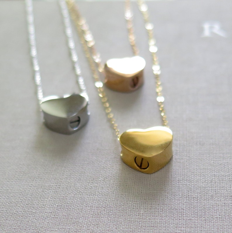 May include: Three heart-shaped necklaces with chains. The necklaces are silver, gold, and rose gold. The hearts are hollow and have a small screw on the side.
