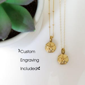 May include: Two gold-toned necklaces featuring sand dollar pendants. One chain has small beads, while the other is a standard link chain. The text "Custom Engraving Included" is printed on the left side of the image.