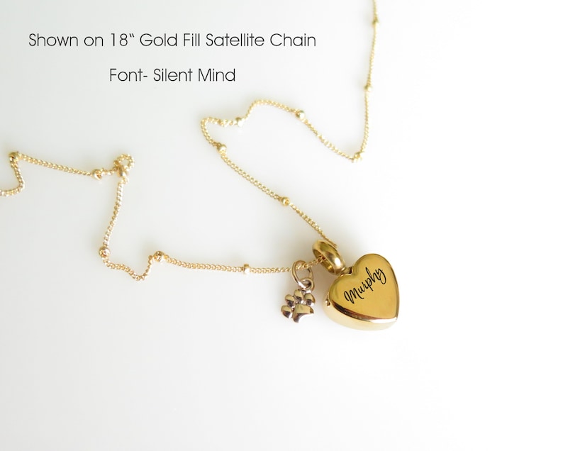 May include: Gold filled satellite chain necklace with a heart-shaped pendant engraved with the name "Murphy" and a small paw print charm. The chain is 18 inches long.