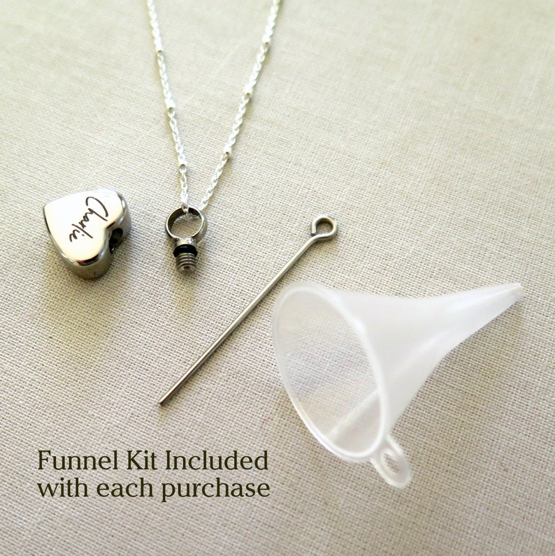 May include: A silver heart-shaped cremation necklace inscribed with the name "Charlie". The necklace is supplied with a funnel kit for filling the pendant.