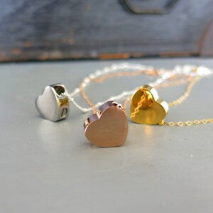 May include: Three heart-shaped pendants on chains, one silver, one gold, and one rose gold.
