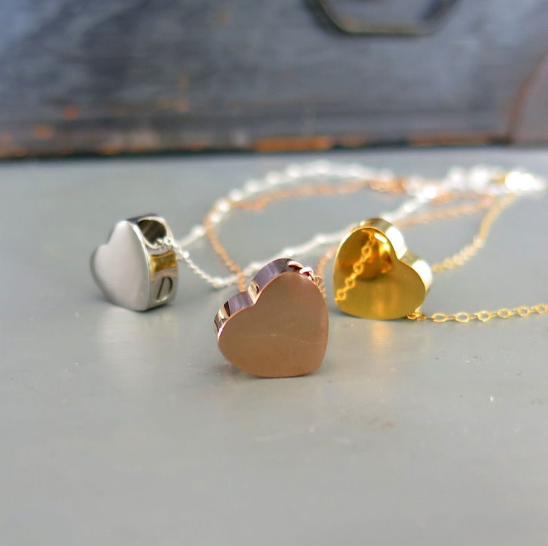 May include: Three heart-shaped pendants on chains, one silver, one gold, and one rose gold.