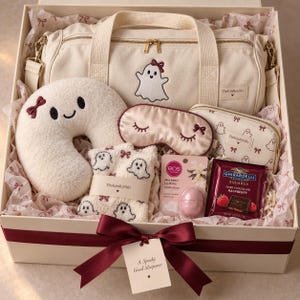 May include: A gift box containing a cream canvas duffel bag with a ghost embroidery, a plush cream ghost-shaped neck pillow, a satin sleep mask, ghost-patterned socks, a vanilla bean lip balm, and a Ghirardelli dark chocolate raspberry square.