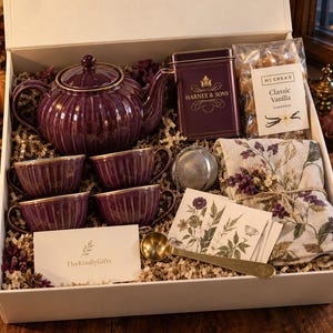 May include: A gift box containing a deep purple ribbed teapot and four matching teacups with gold rims, a Harney & Sons tea tin, a bag of McCrea's Classic Vanilla caramels, a metal tea infuser, a floral print cloth, a gold spoon, and a TheKindlyGifts card.