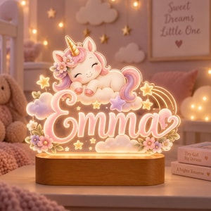 May include: A custom LED night light featuring a sleeping unicorn with a gold horn, pink and purple mane, and flowers, resting on a cloud above the name Emma in cursive script. The design includes stars and sits on a rectangular wooden base.