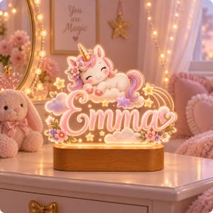 May include: A custom LED night light featuring a sleeping unicorn with a gold horn, pink and purple mane, and floral accents. The light displays the name Emma in cursive script, surrounded by stars and clouds, mounted on a rectangular wood base.