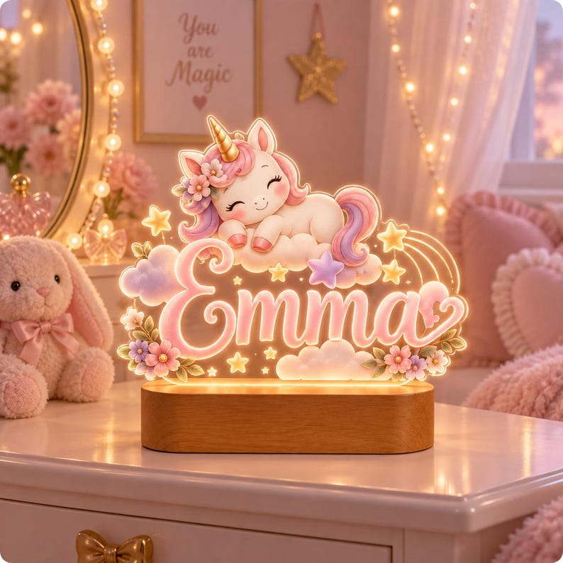 May include: A custom LED night light featuring a sleeping unicorn with a gold horn, pink and purple mane, and floral accents. The light displays the name Emma in cursive script, surrounded by stars and clouds, mounted on a rectangular wood base.