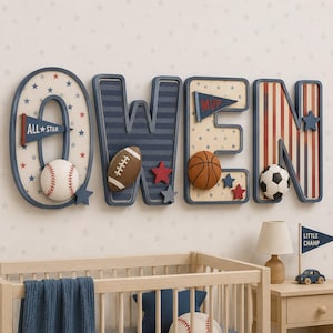 May include: A wall-mounted decorative name sign spelling OWEN in large, navy blue outlined letters. Each letter features sports-themed patterns, including stars, stripes, and pennants labeled ALL STAR and MVP, with attached baseball, football, basketball, and soccer ball accents.