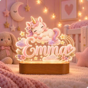May include: A custom LED night light featuring a sleeping unicorn with a gold horn, pink and purple mane, and floral accents, resting on a cloud above the name Emma in script lettering, all mounted on a rectangular wooden base with warm lighting.