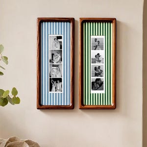 Op de afbeelding: Twee rechthoekige houten lijsten aan een muur. De linkerlijst heeft een lichtblauw en wit gestreepte achtergrond met een verticale strook van vier zwart-witfoto's. De rechterlijst heeft een groen en wit gestreepte achtergrond.