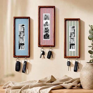 May include: Three rectangular wooden wall-mounted key holders with vertical striped backings in blue, red, and green. Each frame displays a vertical strip of four black and white photographs and features two metal hooks for hanging keys and key fobs.