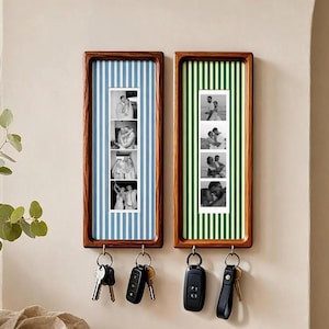 May include: Two rectangular wooden wall-mounted key holders with vertical striped backings in light blue and green. Each frame displays a vertical strip of four black and white photographs and features two metal hooks holding various metal keys.