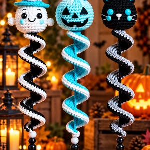 May include: Three hanging crochet ornaments featuring a ghost in a blue hat, a blue pumpkin, and a black cat. Each figure is attached to a spiraling tail of alternating colours, ending in a black witch hat with a blue buckle and white trim.