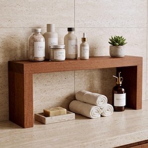 Op de afbeelding: Een rechthoekige houten plank met diverse badkamerartikelen, waaronder Eira badzout, Vera serum, een kleine vetplant in een stenen pot, een stuk zeep in een stenen schaaltje, drie opgerolde witte handdoeken en een bruine glazen fles roomspray.