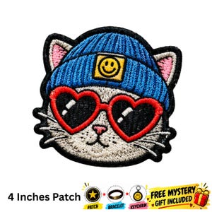 May include: An embroidered patch featuring a white cat wearing a blue knit beanie with a yellow smiley face patch and red heart-shaped sunglasses. The patch measures 10.16 cm in width and height, with a black border and detailed stitching.