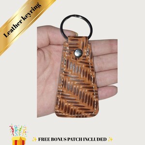 May include: A tan leather keyring featuring a repeating embossed basketweave pattern, white contrast stitching along the edges, a silver-toned metal snap button closure, and a circular metal split ring at the top for attaching keys.