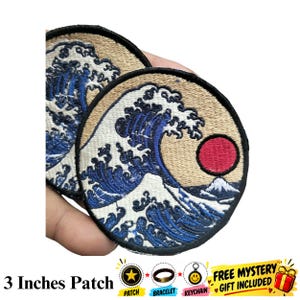 May include: Two circular embroidered patches featuring a depiction of a large blue ocean wave with white foam crests, a red sun, and a small mountain peak against a tan background, each measuring 3 inches in diameter with a black stitched border.