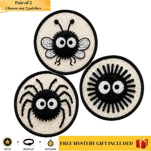 May include: Three circular embroidered patches featuring black and white cartoon characters on a textured cream background. One patch shows a winged insect, one a spider, and one a spiky creature, all with large white eyes and black pupils.