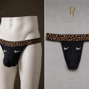 Peut inclure: String noir côtelé doté d'une large ceinture à motif léopard marron et noir. L'avant du tissu noir présente deux petits logos virgule blancs brodés, positionnés de manière symétrique de chaque côté du vêtement.
