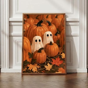 May include: A framed wall art print featuring a collection of orange pumpkins and two white ghost figures with black eyes. The scene is set among fallen autumn leaves in shades of yellow, orange, and red, creating a seasonal harvest display.