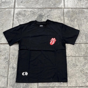 May include: A black short-sleeve t-shirt featuring a small red and white tongue graphic on the chest pocket and the white gothic-style letters CH printed on the lower right side. The shirt has a crew neckline and a standard fit design.