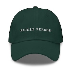 May include: A dark forest green baseball cap featuring the text PICKLE PERSON embroidered in white thread across the front centre. The cap has a structured crown, a curved brim, and a button at the top, showcasing a clean and simple design.