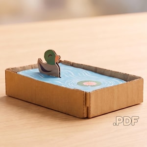 Modèle PDF facile à réaliser d'un canard dans un étang, animal en carton 3D à fabriquer soi-même, activité familiale amusante à télécharger.