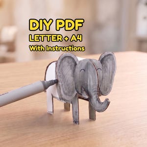 Può includere: Un progetto di bricolage DIY PDF con una figura di elefante grigia realizzata in carta o cartone. Il testo DIY PDF LETTER + A4 With Instructions è visibile sopra l'elefante. Un pennarello grigio colora il lato della figura dell'elefante.