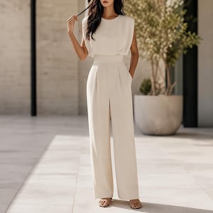 Peut inclure: Une combinaison sans manches de couleur crème avec une encolure ronde, une taille ajustée et un pantalon à jambes larges. Le vêtement présente un design uni et épuré avec des épaules structurées et une texture lisse et uniforme sur l'ensemble.