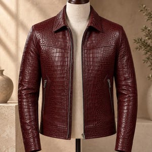 Può includere: Una giacca color bordeaux intenso caratterizzata da una texture con stampa a coccodrillo. Questo capo a maniche lunghe presenta un colletto classico, una chiusura frontale con zip integrale e due tasche verticali con zip all'altezza della vita.