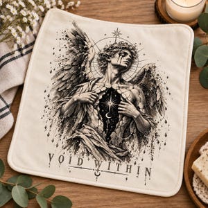 May include: A square off-white fabric cloth featuring a black ink illustration of a winged figure with a cracked torso revealing a starry cosmic void. The text VOID WITHIN is printed at the bottom in a stylized serif font with celestial symbols.