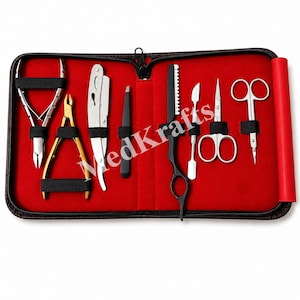 Puede incluir: Un kit de aseo en un estuche negro con cremallera y forro interior rojo. El conjunto incluye herramientas de metal plateado y dorado como alicates para cutículas, una navaja de afeitar, pinzas, un peine de entresacar negro, un bisturí y tijeras.