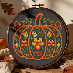 Peut inclure: Un tambour à broder circulaire en bois contenant un tissu gris foncé avec un motif au point de croix représentant une citrouille orange. La citrouille est ornée de fleurs orange et jaunes, de feuilles vertes et de vignes en style pixelisé.