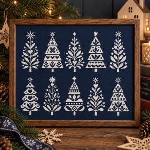 May include: A framed cross-stitch embroidery featuring ten distinct white Christmas tree designs arranged in two rows against a solid dark navy blue fabric background. The trees display various geometric, floral, and heart-shaped patterns.