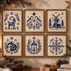 May include: Six square framed cross-stitch artworks featuring dark blue thread designs on a light beige fabric background. The patterns include a goat, two birds, a windmill, a fox, a lantern, and a snowflake, all surrounded by botanical motifs.