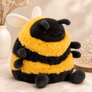 May include: A plush bee toy featuring a round, chubby body with alternating horizontal stripes of fuzzy black and golden yellow fabric. The stuffed animal has two small antennae, two light-colored wings on its back, and four small limbs.