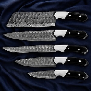 May include: A set of five kitchen knives with hammered Damascus steel blades and black handles. Each knife features a silver-colored bolster with two rivets. The blades display a distinct textured pattern across the metal surface, arranged in a vertical row.