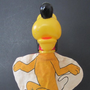 May include: Vintage Pluto hand puppet. The puppet features a yellow plastic head with a black topknot and a red collar. The body is a tan fabric with a Pluto illustration and the name "PLUTO" in red letters.