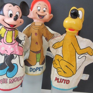 May include: Three vintage Disney character hand puppets: Minnie Mouse, Dopey, and Pluto. Minnie Mouse wears a pink dress with white polka dots. Dopey is in a brown outfit. Pluto is yellow. Each puppet has a white fabric body.