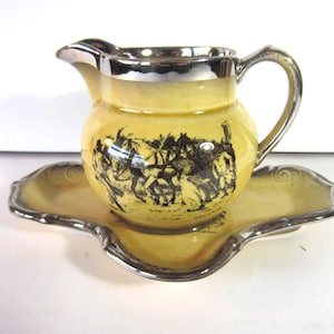 May include: A vintage yellow creamer and saucer set. The creamer has a silver rim and handle, and a black and white illustration of people and horses. The saucer has a silver trim and a scalloped edge.