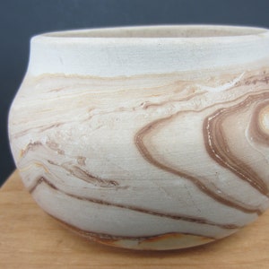 May include: A handmade ceramic bowl with a unique, marbled design. The bowl features a creamy white base with swirling patterns of brown and tan, creating a natural, earthy aesthetic. The bowl is round with a slightly flared rim.