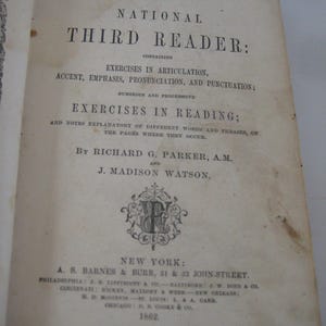 May include: Open book titled "The National Third Reader" from 1862. The cover features black text with the title and author's names. The book contains exercises in articulation, accent, emphasis, pronunciation, and punctuation. The book is open to a page with text.