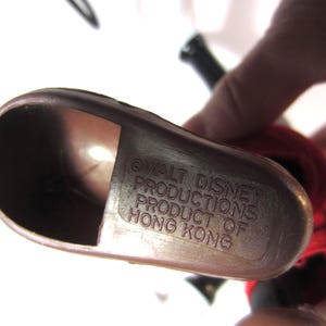 Pode incluir: Um close-up de um objeto de pl&aacute;stico castanho com o texto "WALT DISNEY PRODUCTIONS PRODUCT OF HONG KONG" em relevo na superf&iacute;cie. O objeto tem uma forma curva e parece fazer parte de uma figura maior.