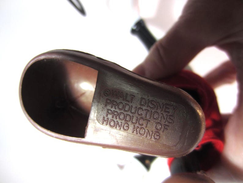 Pode incluir: Um close-up de um objeto de pl&aacute;stico castanho com o texto "WALT DISNEY PRODUCTIONS PRODUCT OF HONG KONG" em relevo na superf&iacute;cie. O objeto tem uma forma curva e parece fazer parte de uma figura maior.