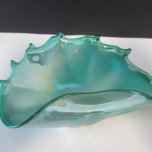 May include: A teal-colored glass bowl with a unique, organic shape. The bowl has a rippled edge with pointed tips, and the glass has an iridescent sheen. The bowl is likely used for decorative purposes.