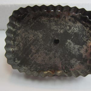 May include: A vintage, oval-shaped metal cookie cutter with a crimped edge. The cutter has a dark, aged appearance with a small hole in the center, suggesting it's been used for baking. The metal has a worn, rustic look.