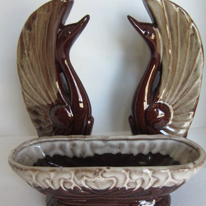 May include: A set of vintage ceramic swan figurines in shades of brown and beige. The set includes two swan wall hangings and a matching oval planter with a decorative rim. A classic home decor item.