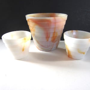 May include: Three white and orange swirled glass planters of varying sizes. The largest planter is in the center, with two smaller planters on either side. The planters have a ribbed design and a marbled appearance.