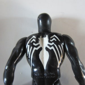 May include: Black action figure of a superhero with a white spider emblem on the back. The figure has a glossy finish and muscular arms. The figure is a collectible toy.